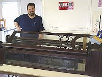 This clock case sets the record for being the largest clock we've seen upstairs in the Educational building. This Herschede tall case clock had a dull finish and some loose parts. Scott Lemke relaxes after a job well done.