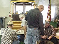 Russ Aikins and Mike Brazil talk about soldering tabs onto a clock bezel while Larry Grubb and Phil Ball discuss their skeleton clock project.